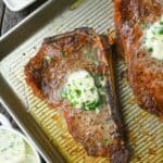 Bone in new york steak on a baking sheet with herbed butter on top.