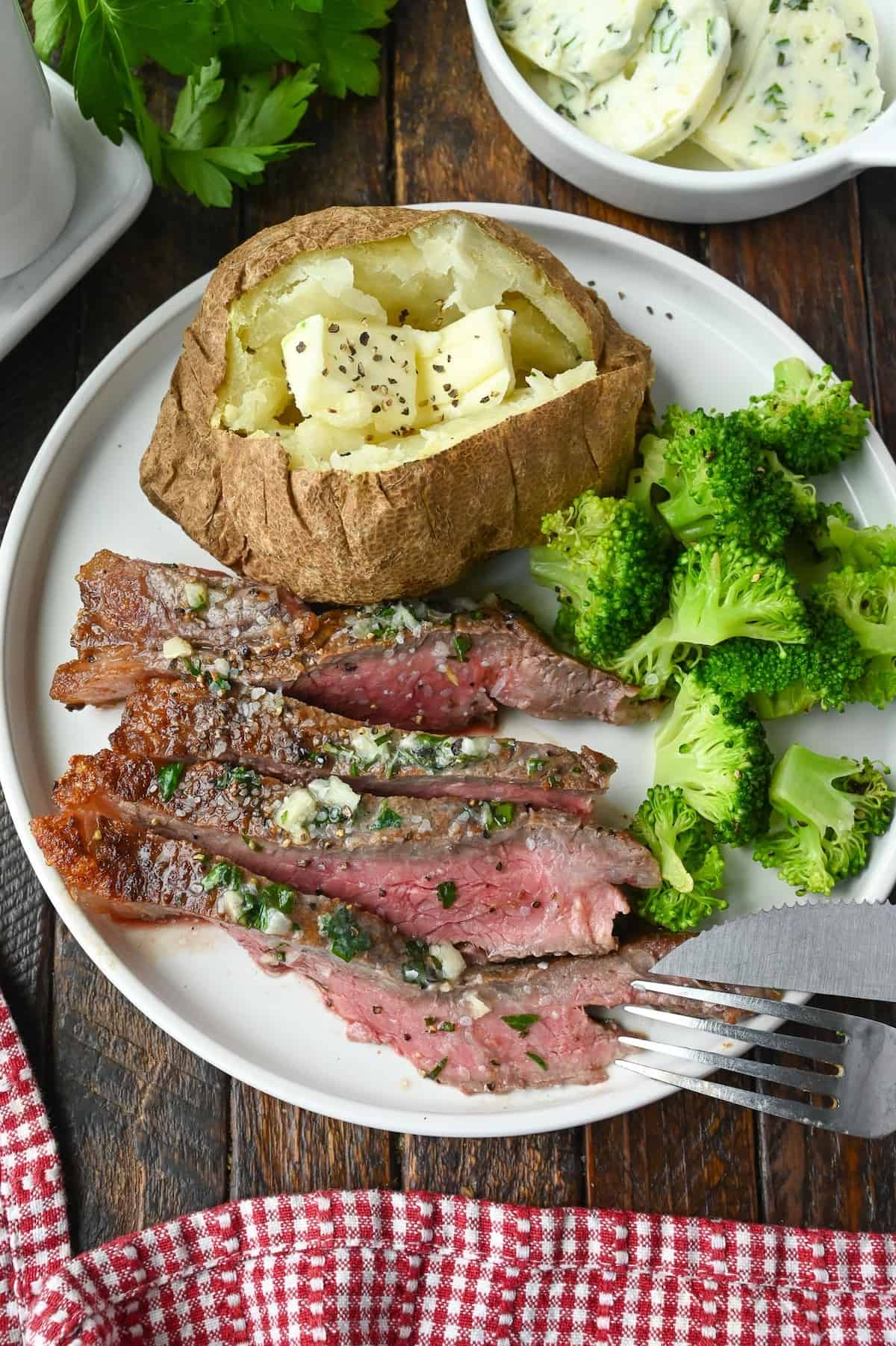 Sliced broiled steak on a plate with a baked potato and broccoli.