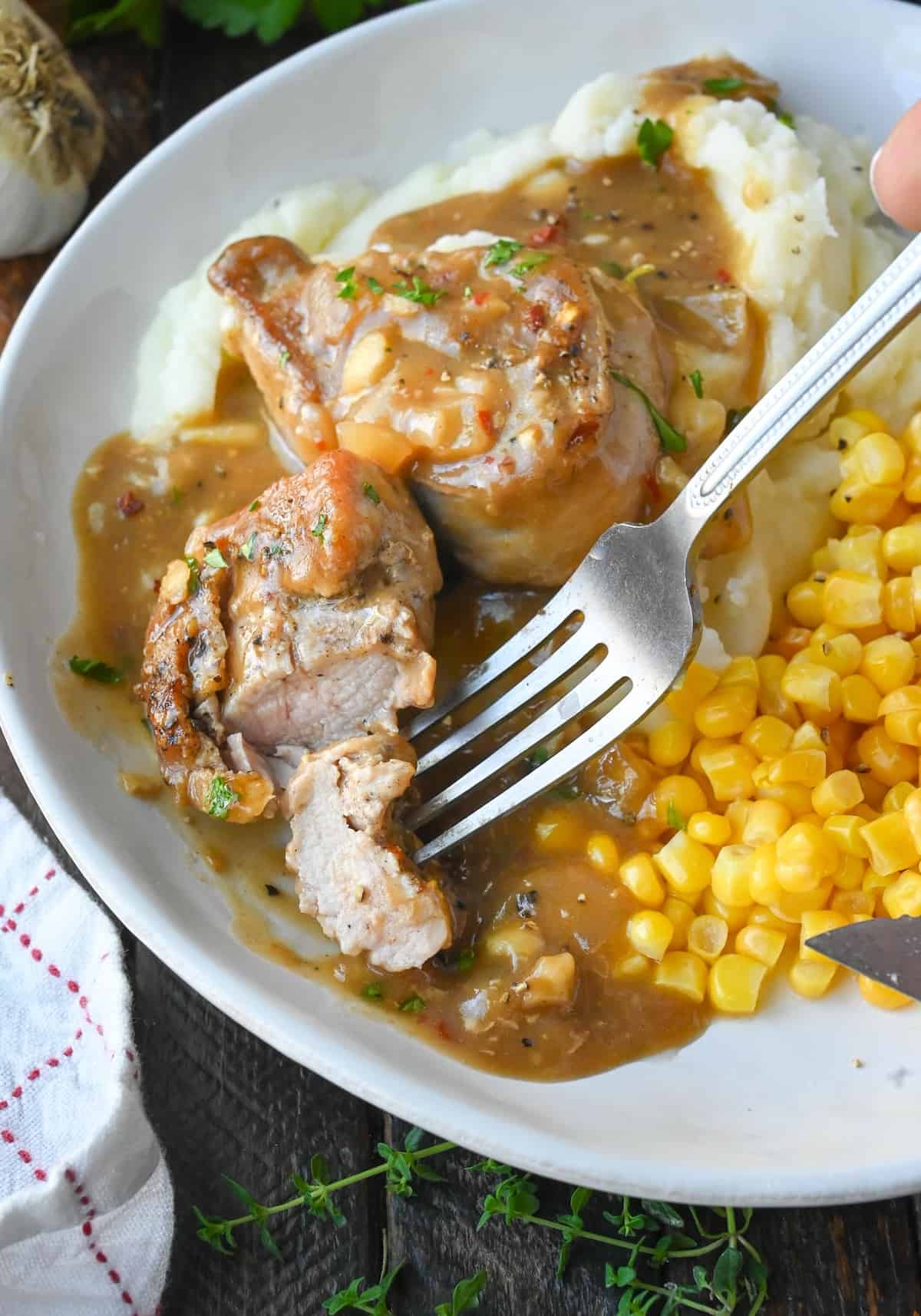 Vertical image of a form grabbing a bite of pork medallions with gravy.