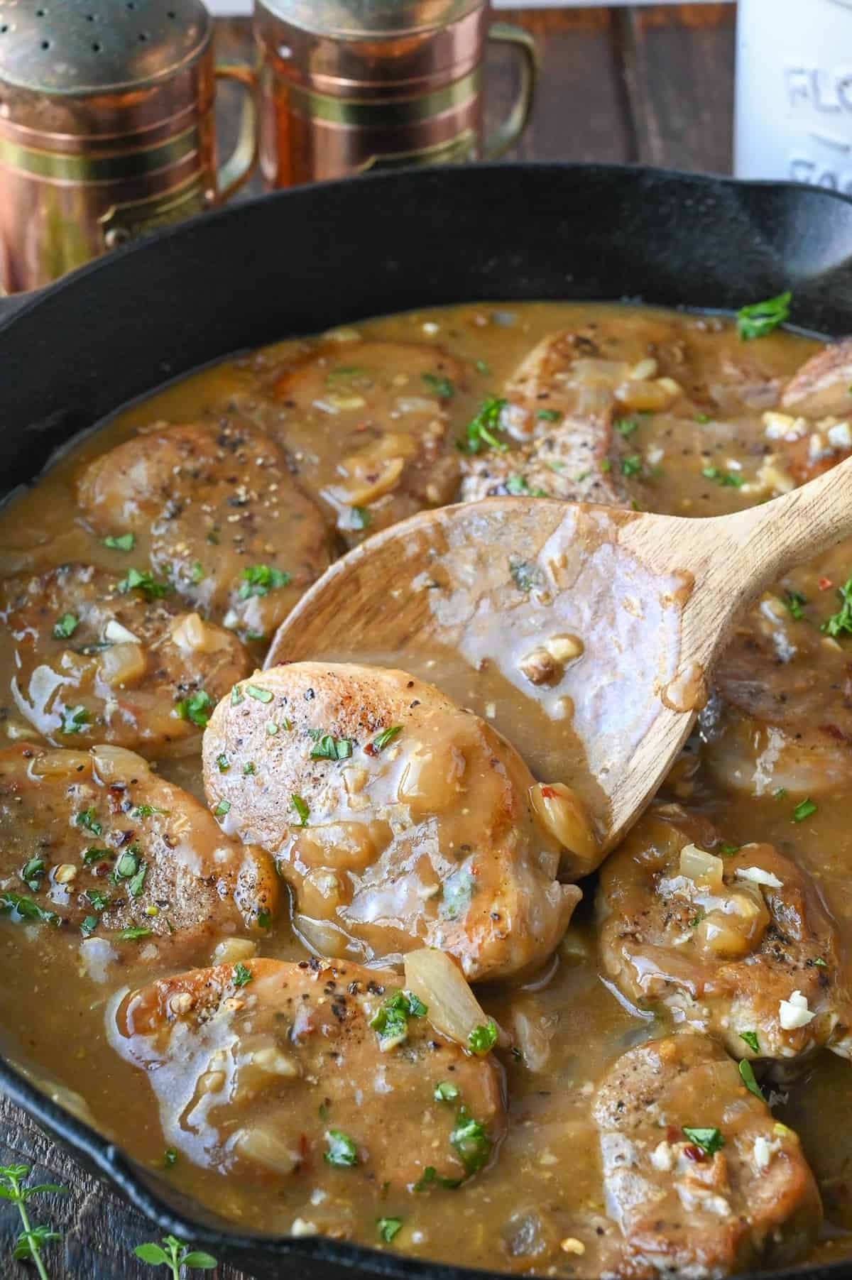 Using a wooden spoon to mix pork medallions in gravy.