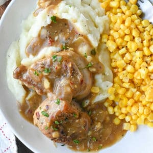 Close up shot of pork medallions with gravy over mashed potatoes and corn.