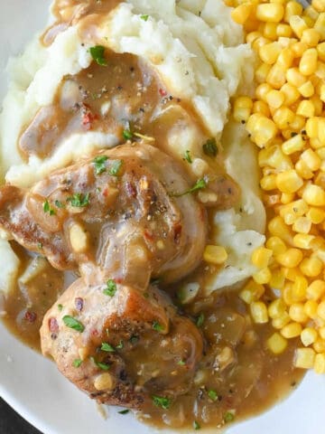 Close up shot of pork medallions with gravy over mashed potatoes and corn.