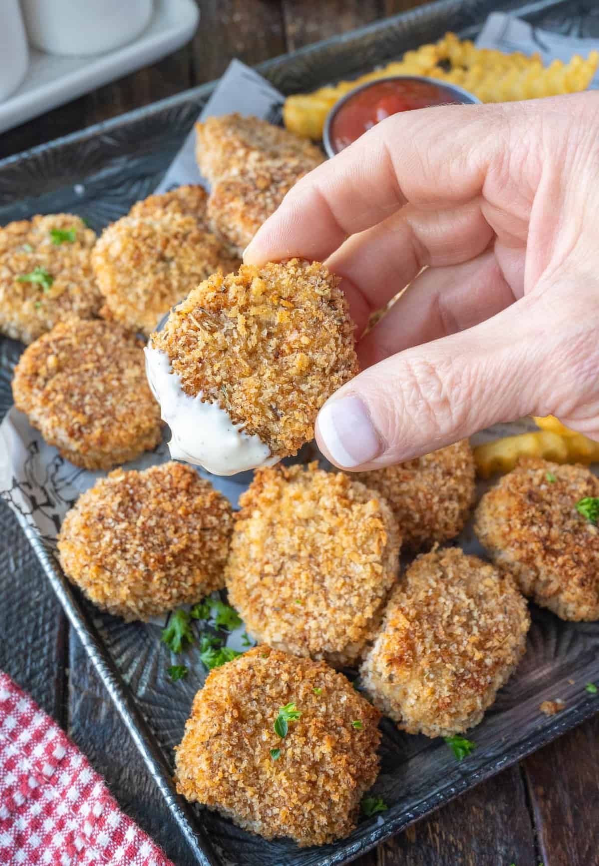 A hand holding a chicken nugget dipped in ranch dressing.