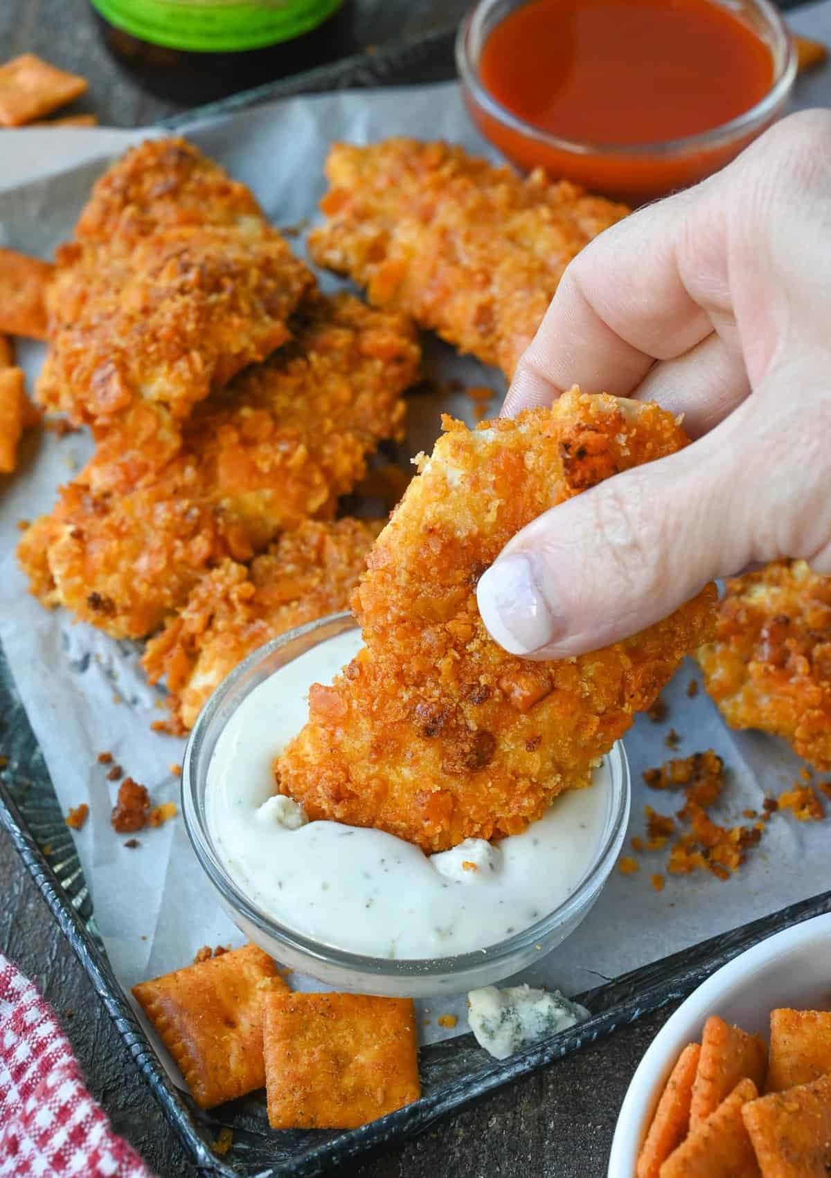Image of a hand dipping a buffalo chicken tender into a dish of blue cheese dressing.