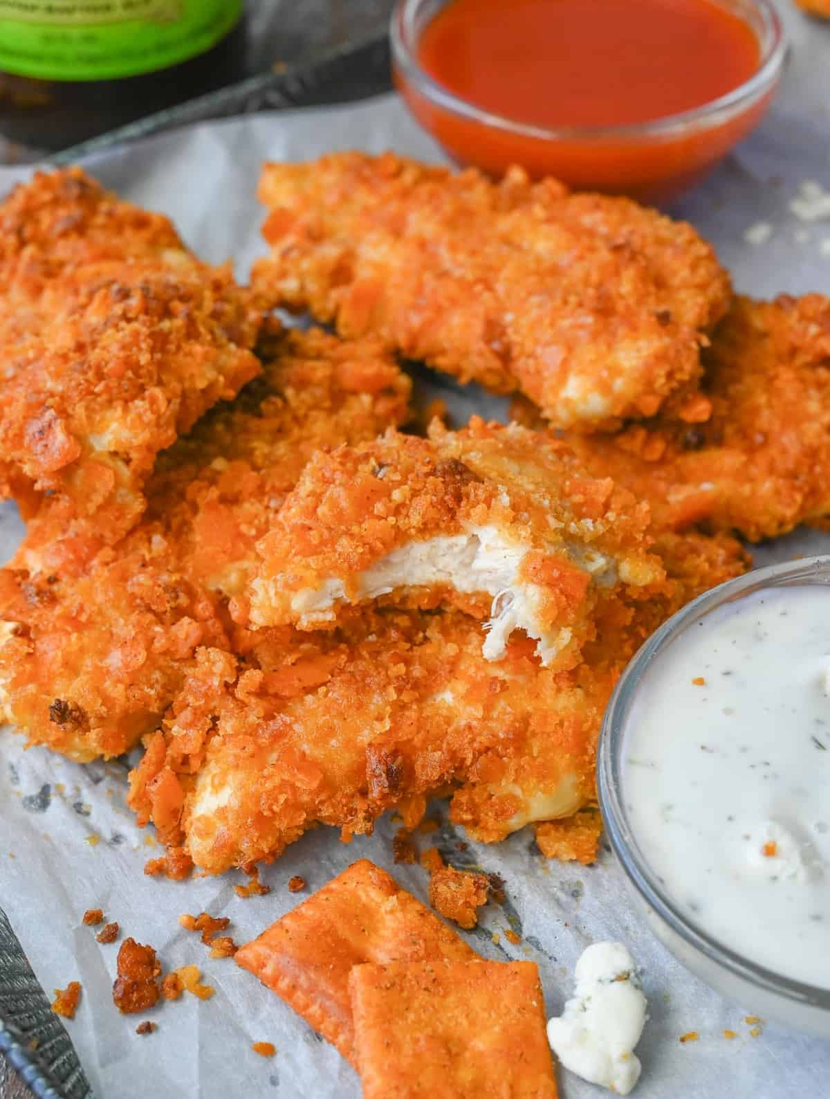 A tray of buffalo chicken tenders and sauces. One tender has a bite taken out of it.