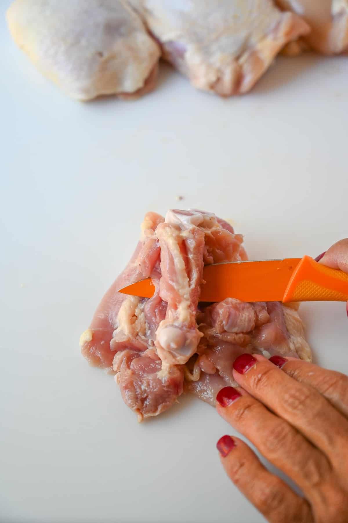Sliding an orange knife underneath the center bone of a chicken thigh.