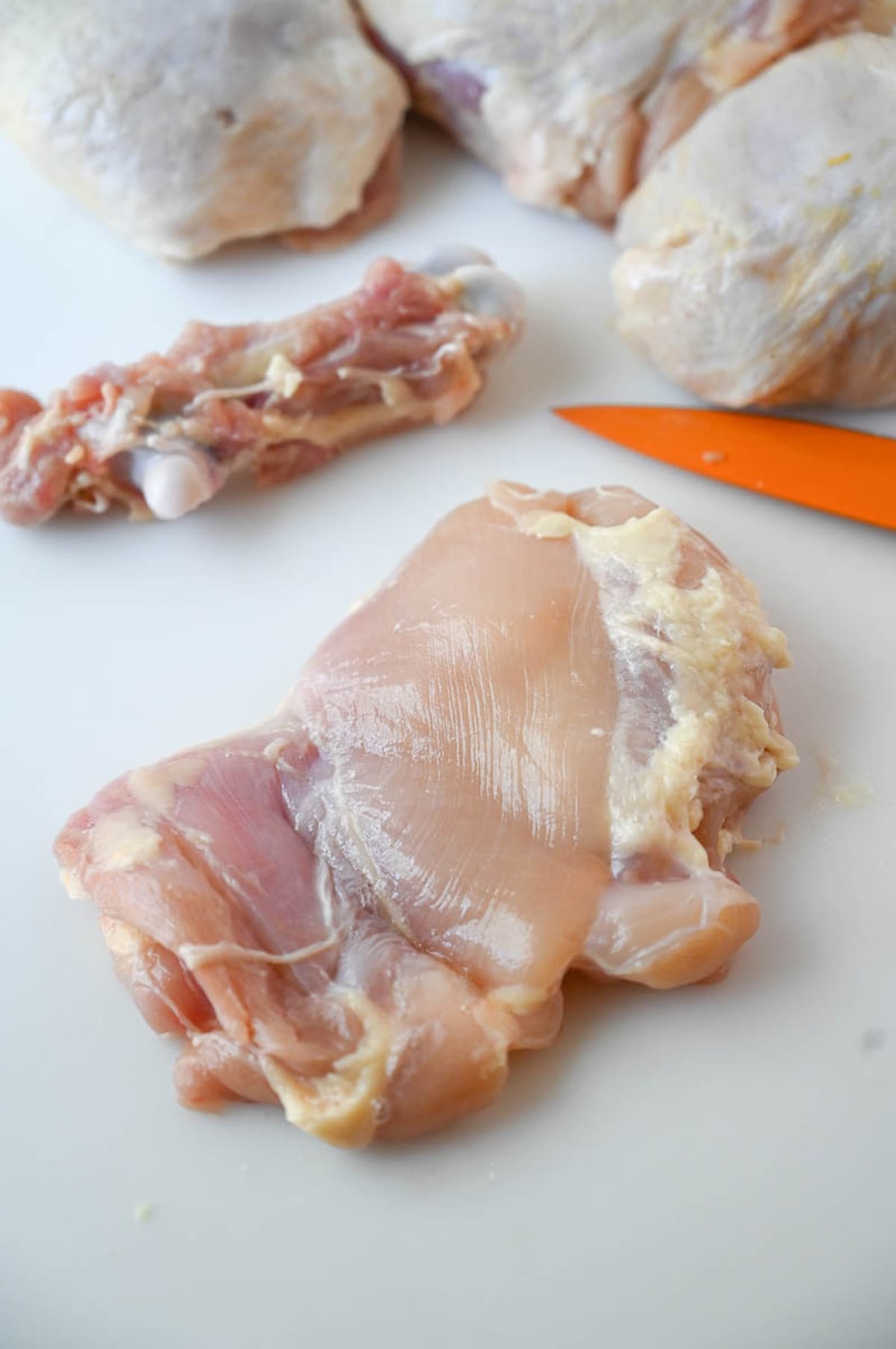 A deboned chicken thigh on a cutting board with the removed bone in the background.