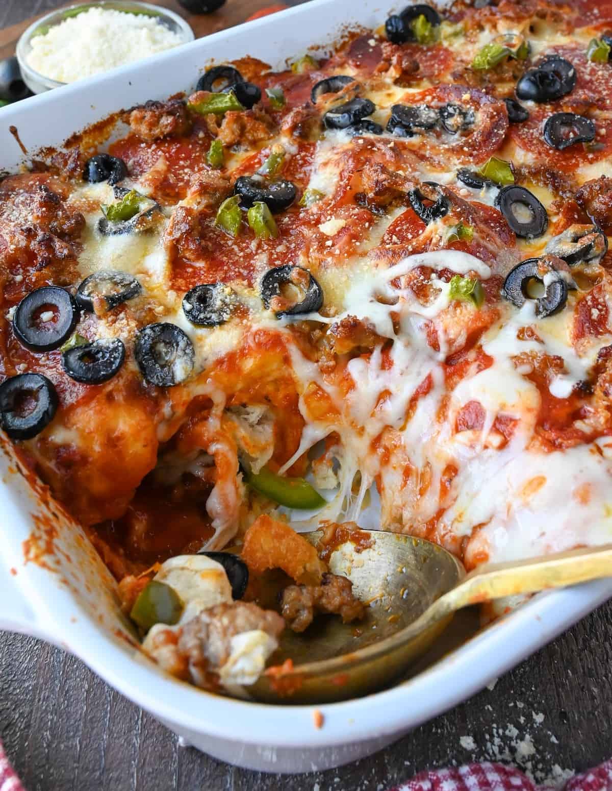 A spoon resting in a casserole dish filled with pizza bake.