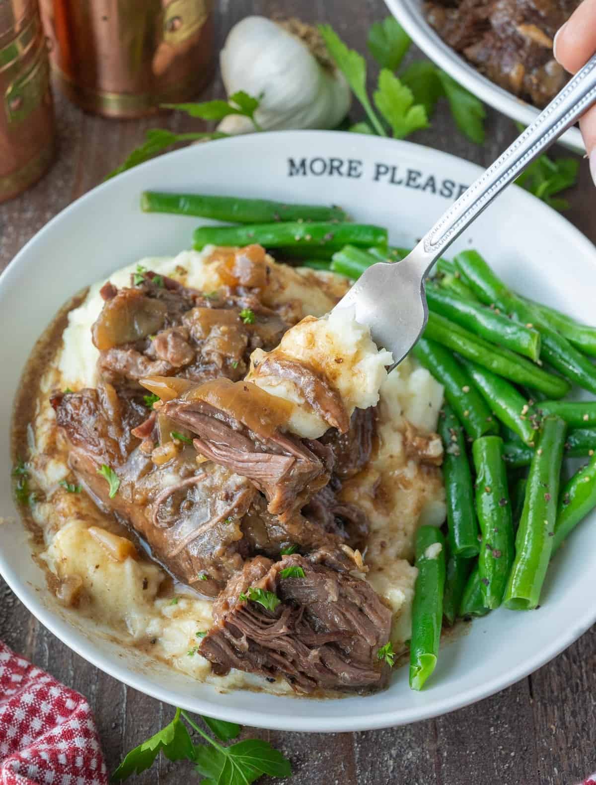 A fork scooping up a bite of beef and gravy with mashed potatoes.