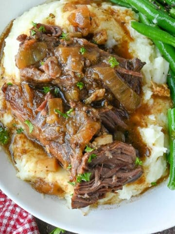Beef and gravy on top of mashed potatoes with a side of green beans.