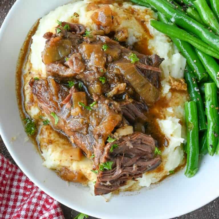 Beef and gravy on top of mashed potatoes with a side of green beans.