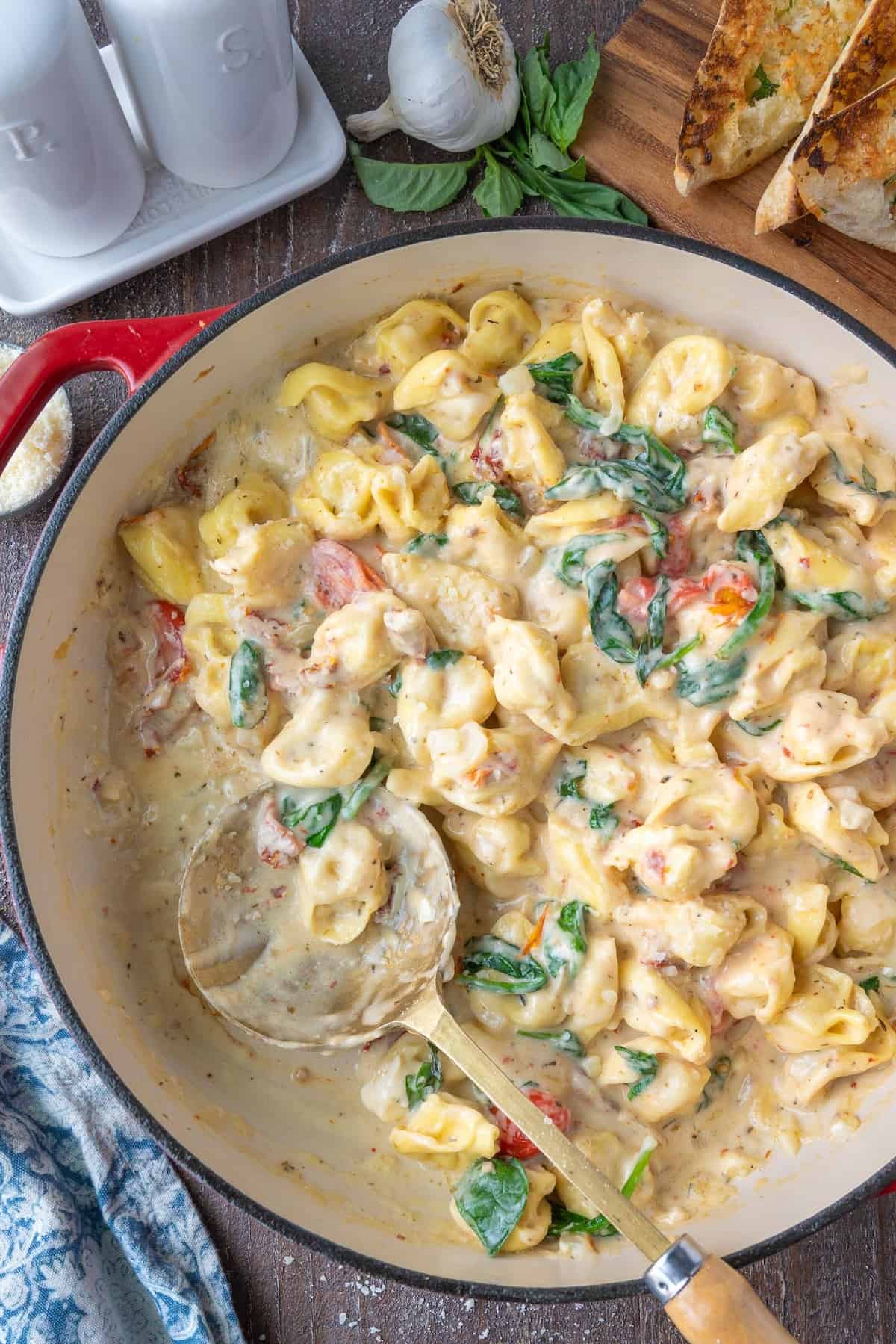 Tuscan tortellini in a skillet with a serving spoon.