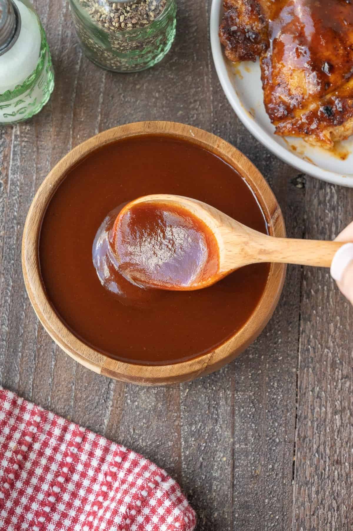 A wooden spoon in a bowl of BBQ sauce.