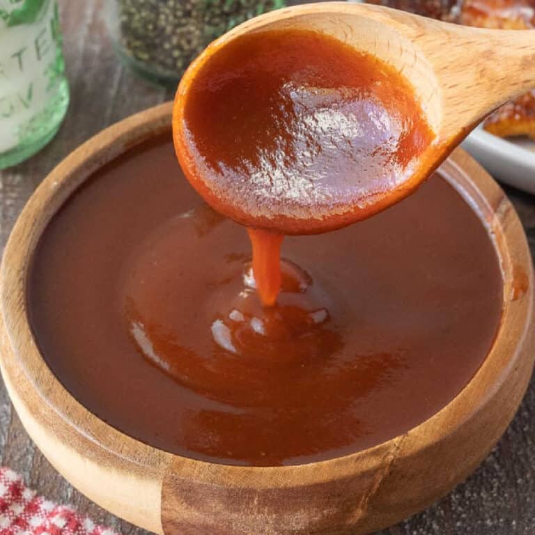 Close up of a wooden spoon drizzling BBQ sauce into a wooden bowl.