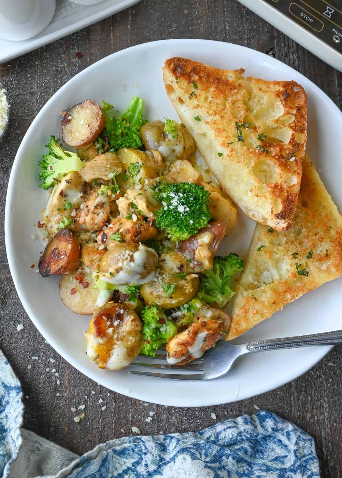 Slow cooker garlic parmesan chicken and potatoes on a plate with garlic bread.