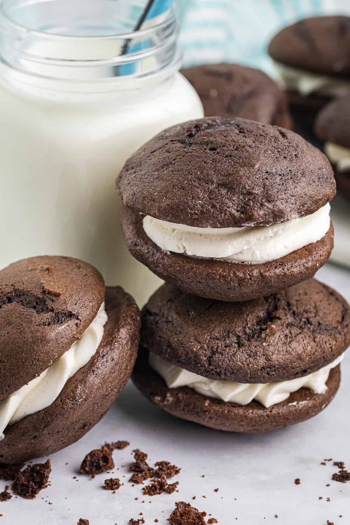 Vertical image of three cake mix whoopie pies, twos tacked on top of each other next to a glass of milk.