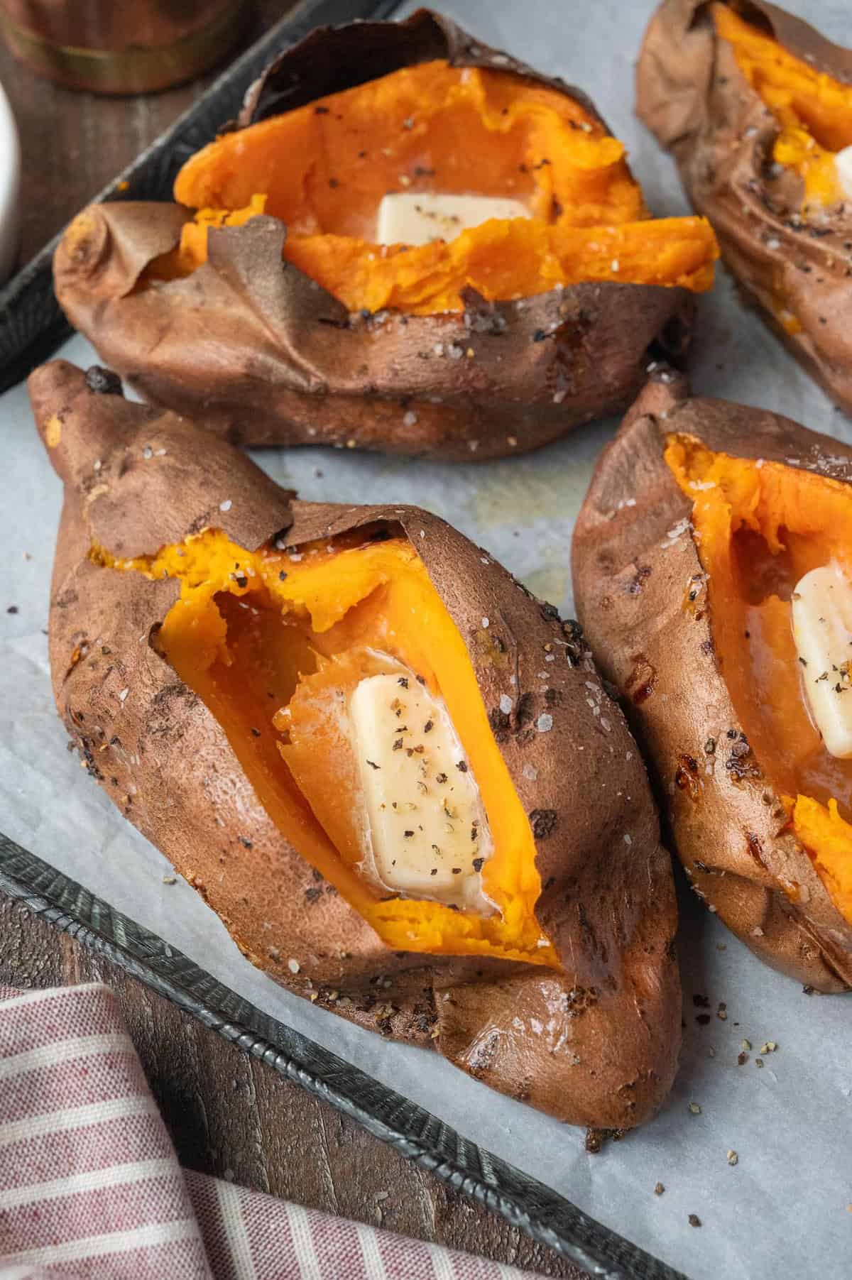 Vertical image of air fryer baked sweet potatoes with butter.
