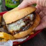 Close up of a hand holding half a tri tip sandwich.