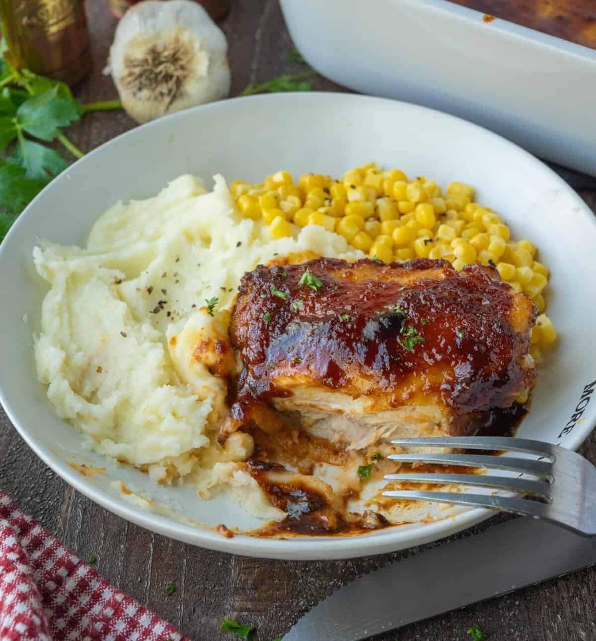 A plate of sticky BBQ chicken with mashed potatoes and corn.