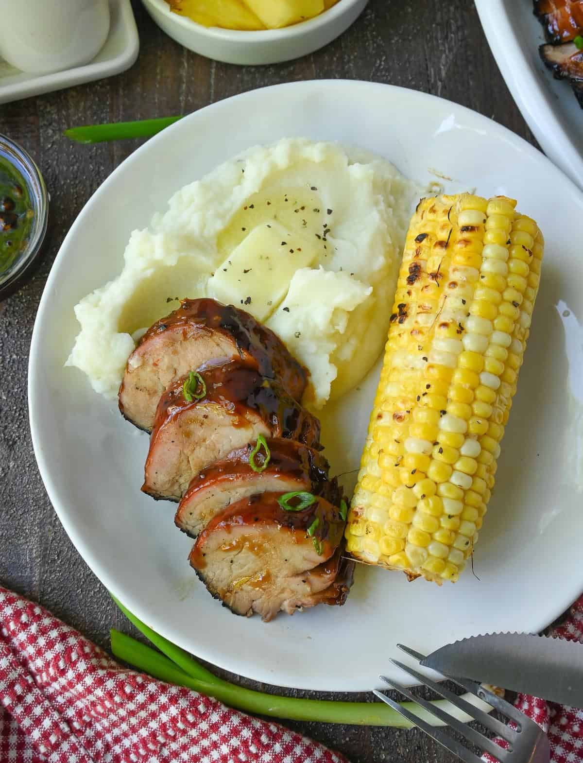 Pork tenderloin, mashed potatoes and corn on the cob on a plate.