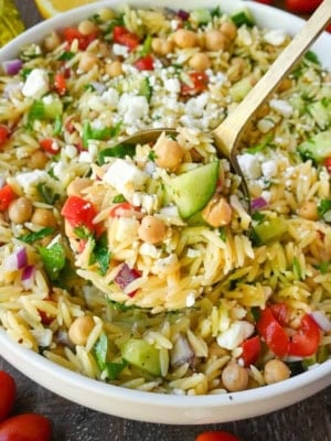 A serving spoon scooping up some chickpea orzo pasta.