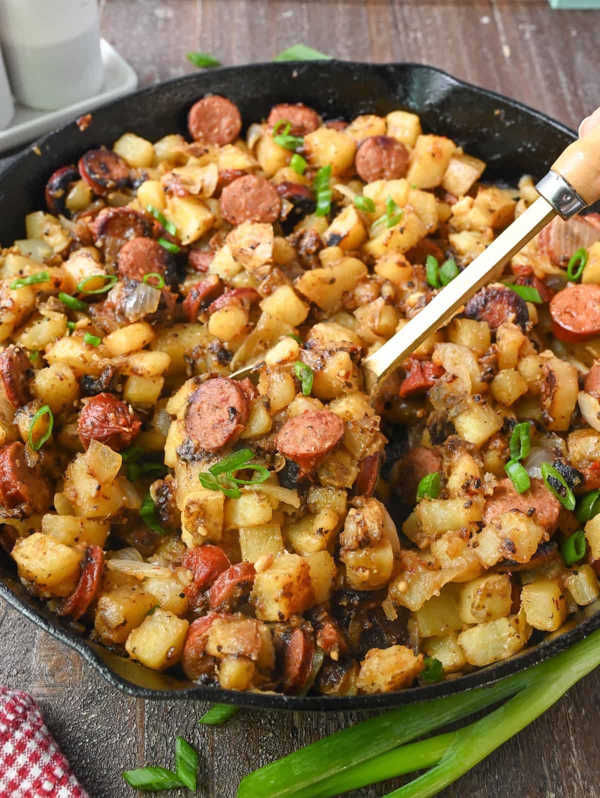 A spoon scooping out some fried potatoes from a skillet.