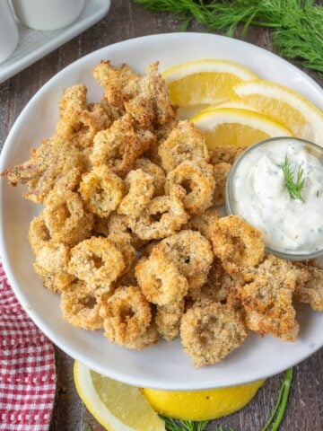 Air fryer calamari on a white plate with lemon slices.