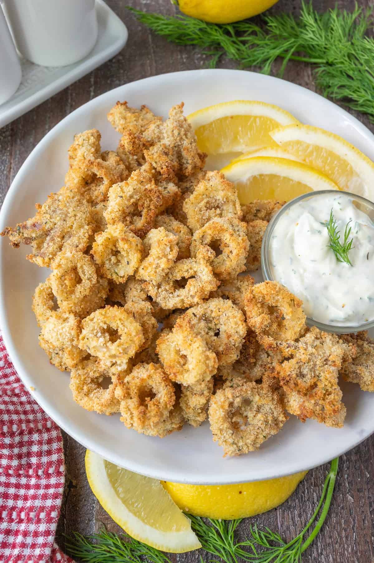 Air fryer calamari on a white plate with lemon slices.