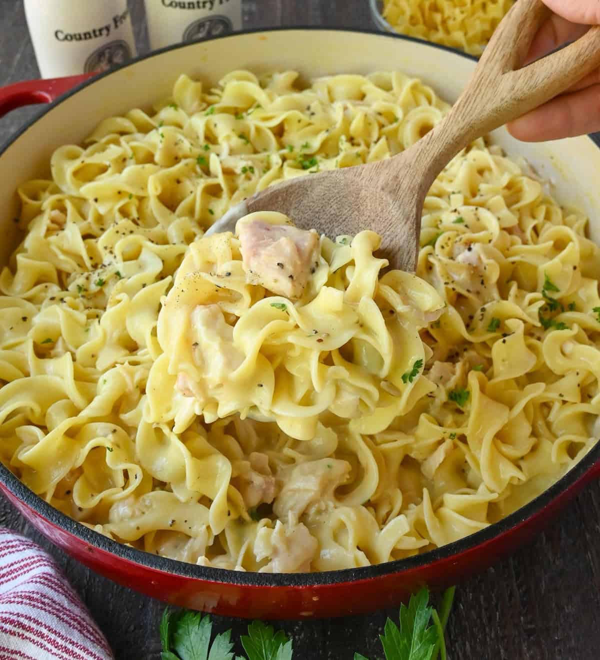 Using a wooden spoon to stir chicken and noodle skillet.