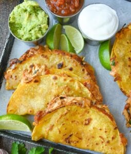 Crispy chicken tacos on a baking sheet with lime slices.