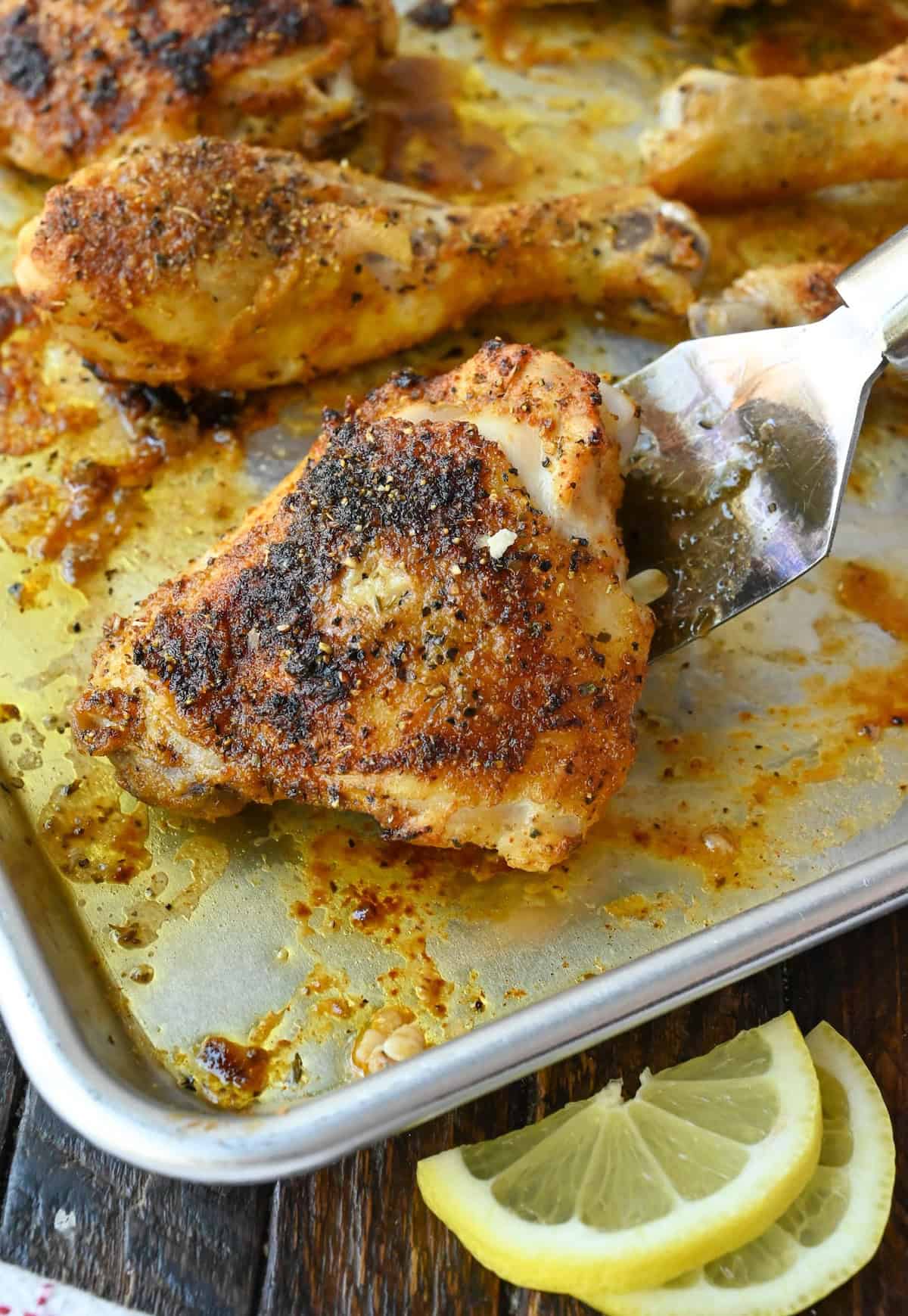 Lifting up a piece of lemon pepper chicken from a baking sheet with a spatula.