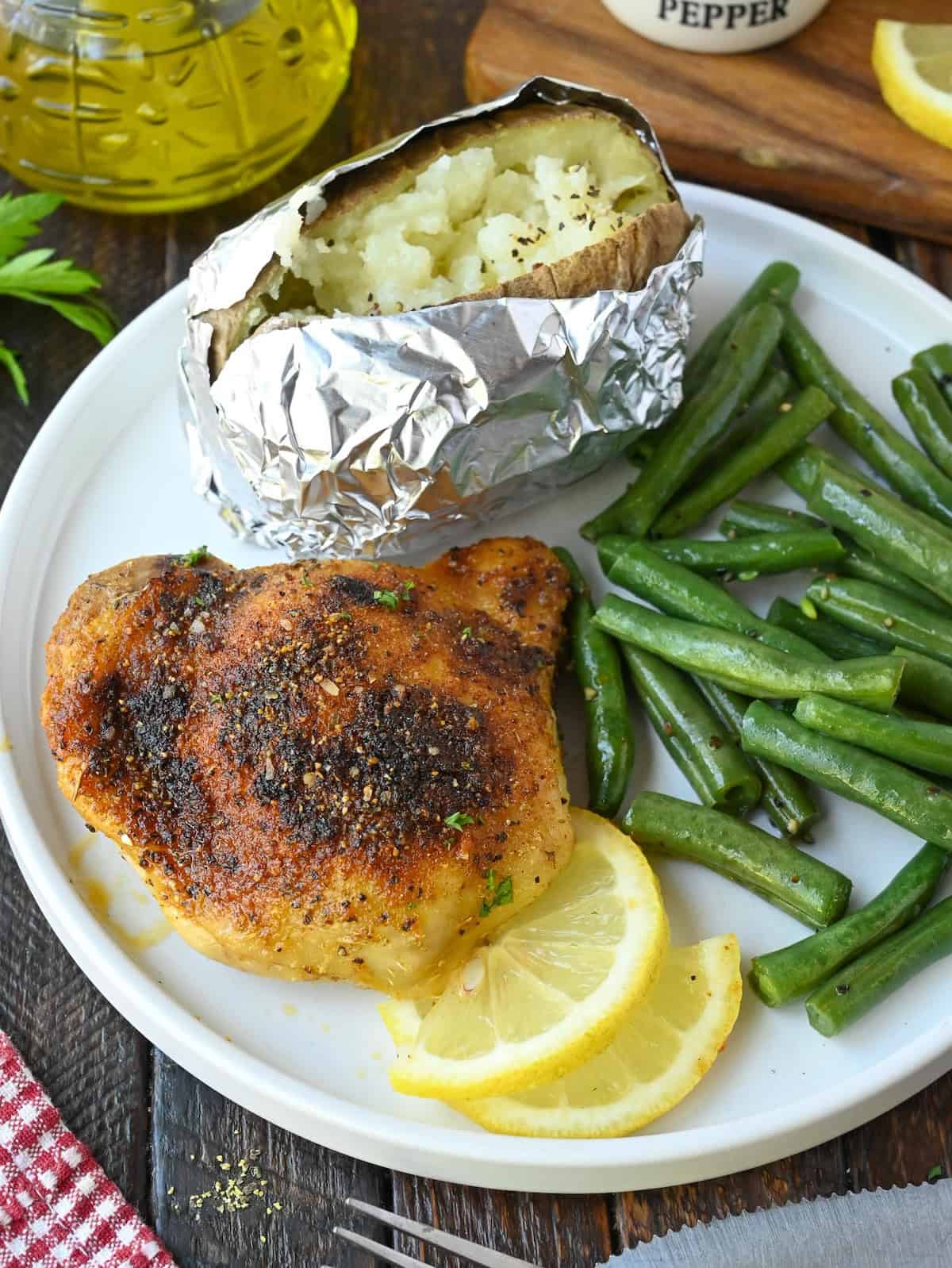 A plate with lemon pepper chicken served with green beans and a baked potato.