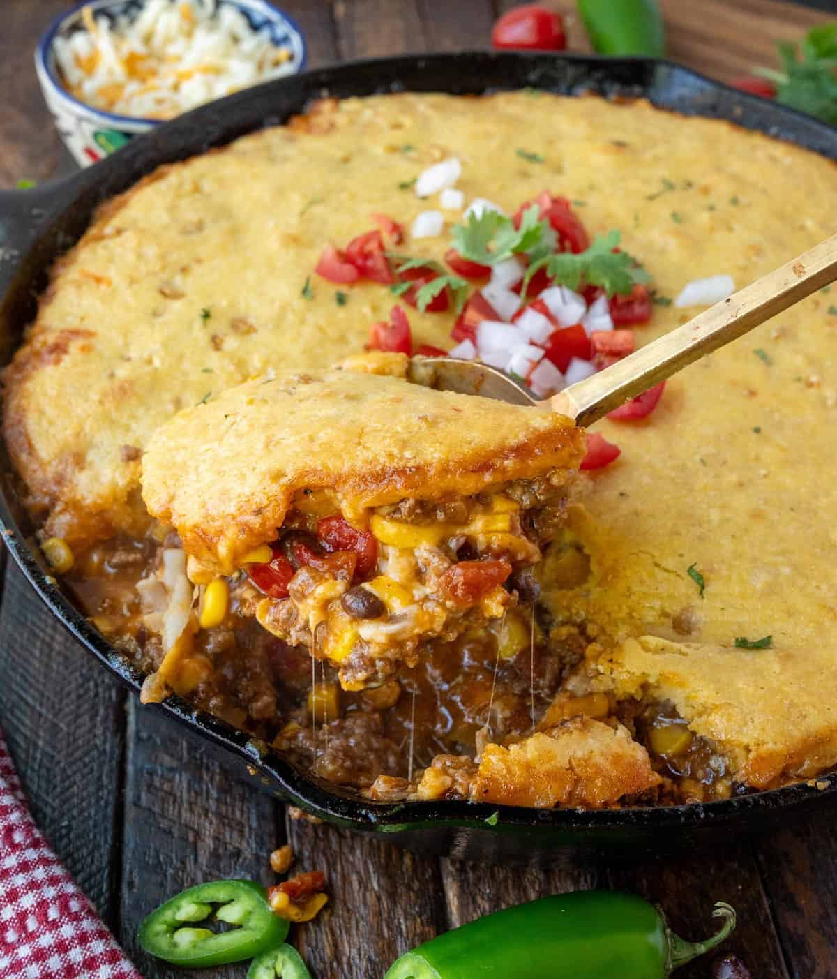 Taking a scoop of cowboy cornbread casserole from a skillet.