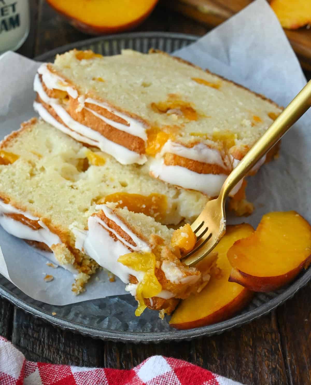 Peach loaf cake on a plate with a fork taking a bite out of it.