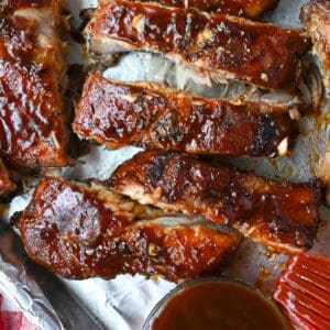 Dr pepper ribs on a baking sheet with a side of bbq sauce.