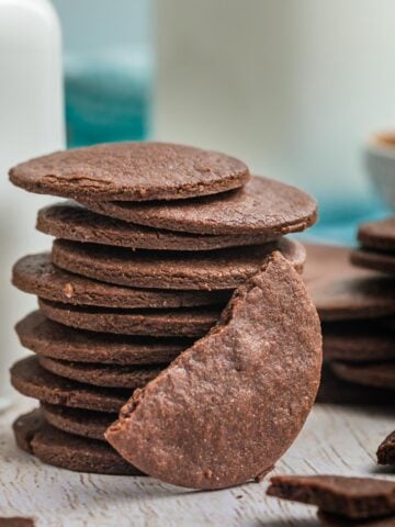 A stack of chocolate wafer cookies with one broken in half and leaning against the stack.