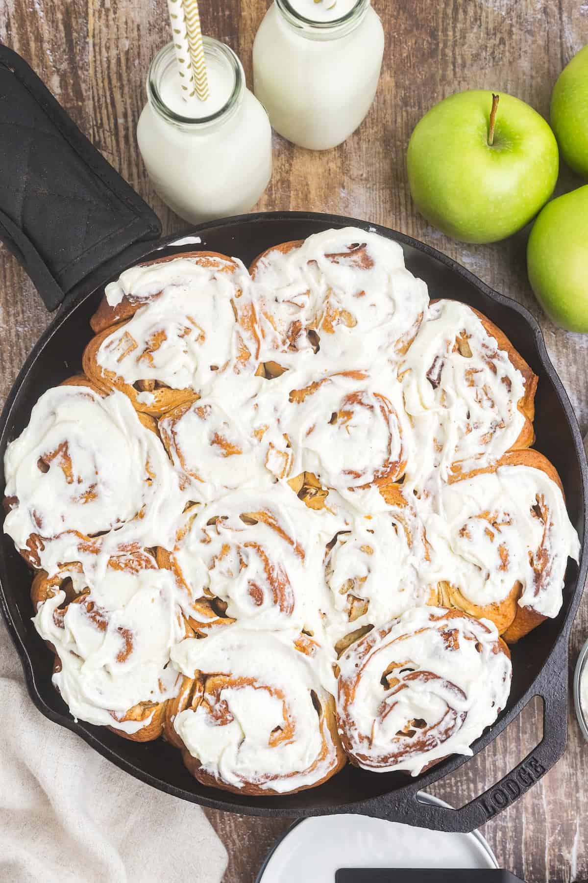 Overhead view of a skillet full of iced apple pie cinnamon rolls.