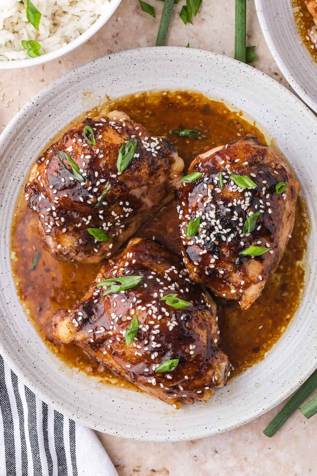 Overhead view of 3 baked teriyaki chicken thighs in sauce on a plate.