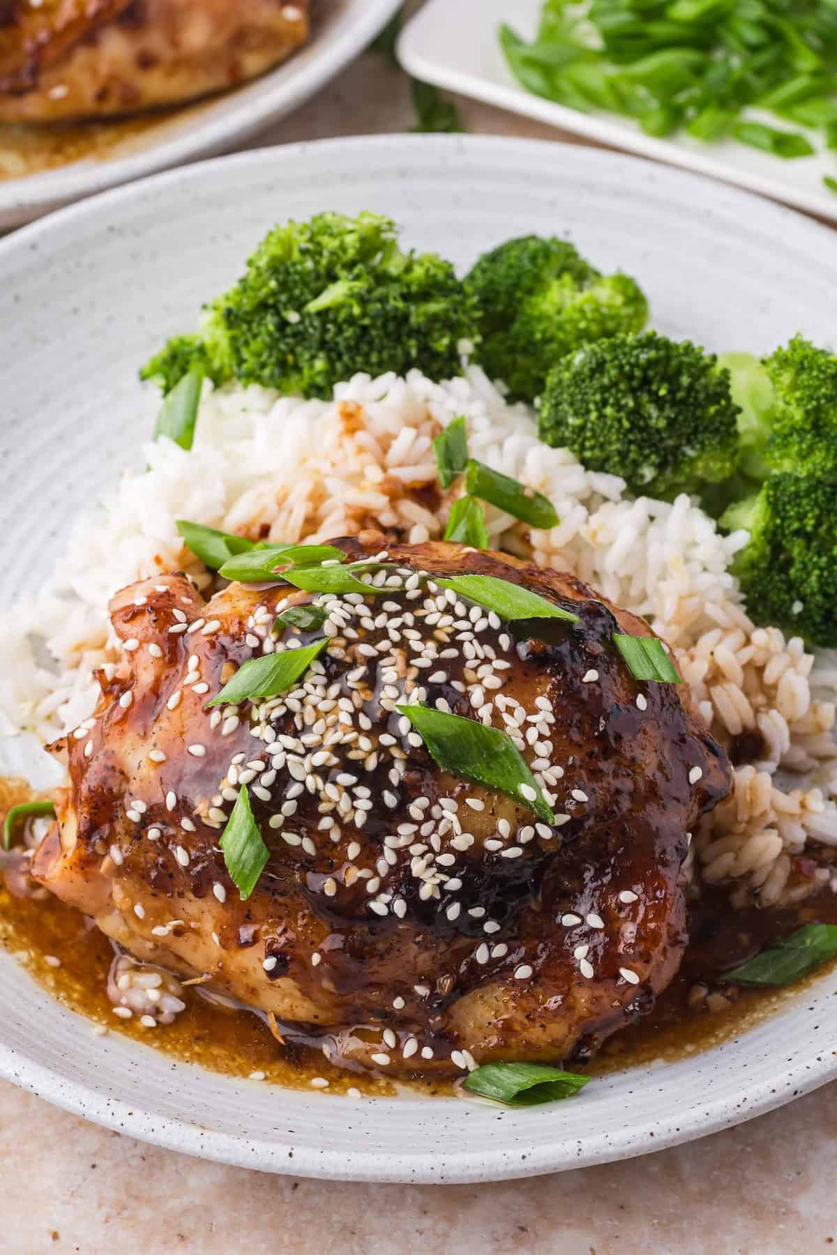 Teriyaki chicken thigh on a plate with rice and broccoli.