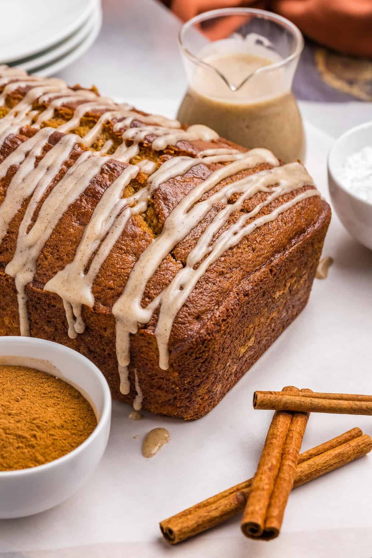 A loaf of pumpkin pound cake on a table with cinnamon and glaze.