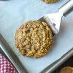 A close up of a spatula lifting a pumpkin spice cookie from a baking sheet.
