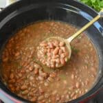 Using a spoon to stir a crock pot of pinto beans.