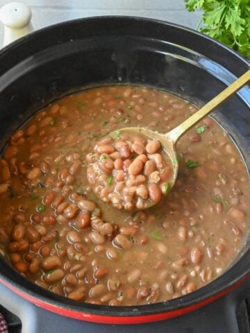 Using a spoon to stir a crock pot of pinto beans.