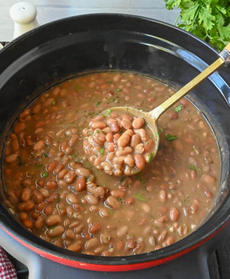 Using a spoon to stir a crock pot of pinto beans.
