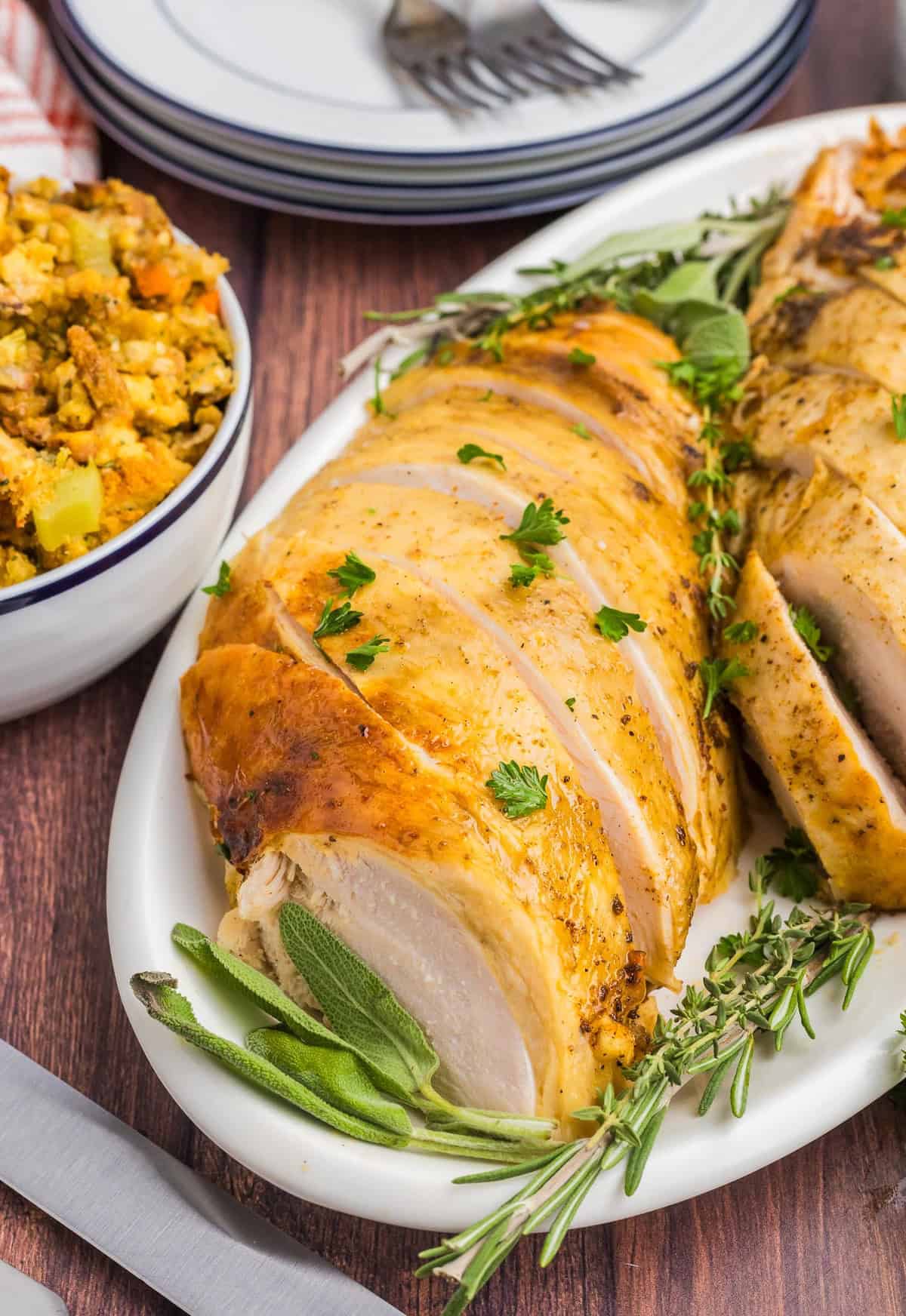 A plate of sliced slow cooker turkey next to a bowl of stuffing.