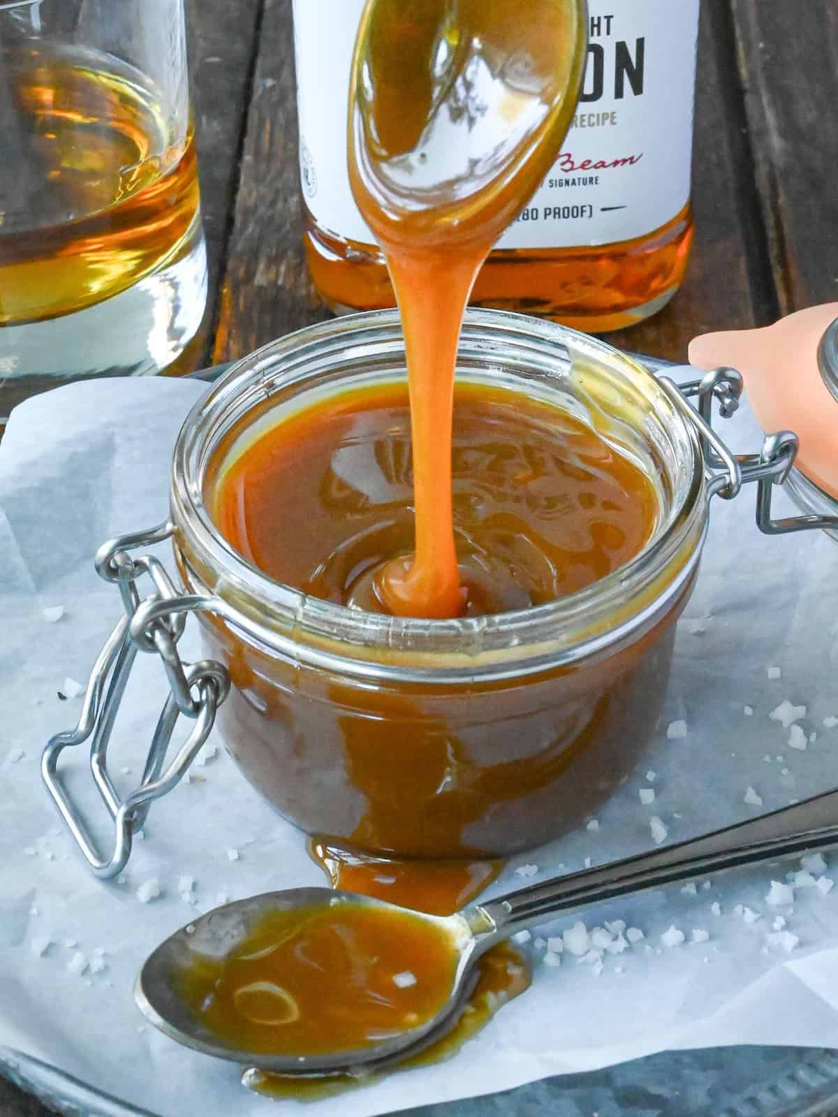 Spooning bourbon caramel sauce out of a glass container.