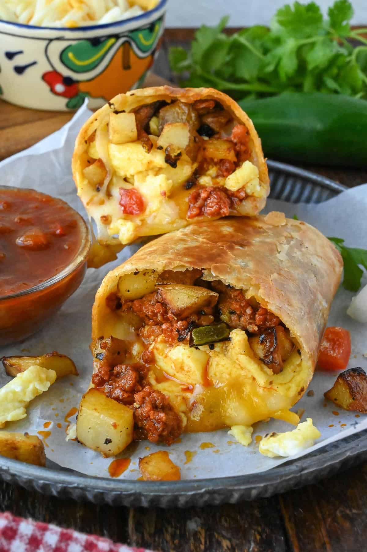 A breakfast burrito cut in half, one half stacked on top of the other, next to a dish of salsa.