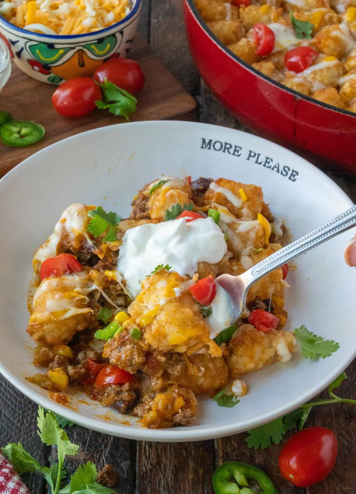 A bowl of tater tot casserole garnished with tour cream and cilantro.