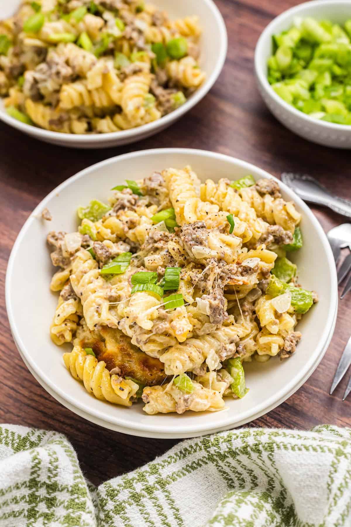 A bowl full of philly cheesesteak pasta casserole garnished with green onion.