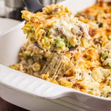 Taking a scoop of cheesesteak casserole from a baking dish.